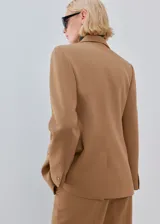 Blazer de corte sastrero en color tostado, con solapas clásicas, cierre frontal de dos botones y bolsillos laterales con solapa.
