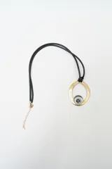 Collar de diseño moderno con cordón negro doble, dije circular grande en tono dorado con acabado irregular y un dije central más pequeño en tono plateado con una piedra oscura engarzada.
