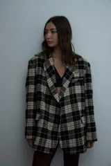 Blazer de corte oversize con estampado de cuadros en tonos negro y beige. Presenta solapas clásicas, cierre frontal con botones y bolsillos laterales con solapa.