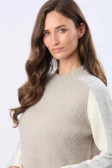 Buzo tejido de abrigo con cuello redondo y manga larga. Presenta un diseño de bloques de color en tonos gris claro y beige.