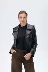 Chaqueta tipo biker de cuero negro con cierre frontal asimétrico, solapas con broches metálicos, bolsillos laterales con cierre y detalles de costuras acolchadas en la parte inferior.