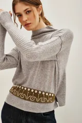 Polera de lana y cachemira color gris, con cuello alto y mangas largas con textura acanalada. Presenta un diseño holgado con aberturas laterales en el ruedo.