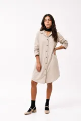 Vestido camisero de corte recto y largo midi, confeccionado en tela de color beige. Presenta cuello clásico, cierre frontal con botones y mangas tres cuartos.