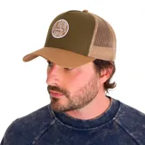Gorra tipo trucker con frente y visera en color verde oliva y marrón, con panel trasero de malla en color beige. Presenta un parche circular bordado en el frente con el texto 'A Tractor Quality Company' y cierre ajustable snapback.