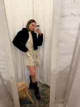 Mono corto de lino color beige, con cuello camisero, cierre frontal, mangas largas abullonadas y cinto ajustable en la cintura.