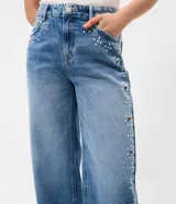 Pantalón wide leg de tiro bajo confeccionado en jean de algodón, con diseño amplio y aplicación de tachas y ojalillos metálicos a lo largo de los laterales.