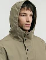 Gabardina con capucha de corte recto y largo medio. Cuenta con cierre frontal engomado, cartera con botones a presión, bolsillos laterales y tejido repelente al agua y al viento.