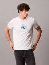 Remera de algodón de corte regular, color beige, con cuello redondo y estampa frontal con el monograma de Calvin Klein sobre un recuadro celeste.