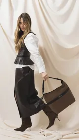 Cartera tipo hobo de tamaño grande en color beige, con detalles en negro. Presenta una franja horizontal negra con el logo de la marca, asa corta de hombro y correa larga desmontable. Incluye bolsillo frontal con cierre oculto y bolsillo trasero.