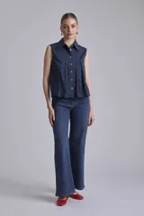 Camisa azul marino sin mangas con cuello clásico, abotonada al frente y detalle de plisados verticales en el pecho.