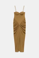 Vestido largo color tostado con diseño estilo corsé, escote corazón con aros y tirantes finos. Presenta un corte ajustado en la cintura con detalle de frunces laterales que aportan volumen a la falda.
