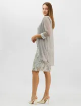 Conjunto de dos piezas compuesto por un vestido midi de silueta recta con tejido plisado metalizado y escote redondo con pedrería, acompañado por una chaqueta de gasa abierta con caída en cascada y mangas tres cuartos con puños metalizados.