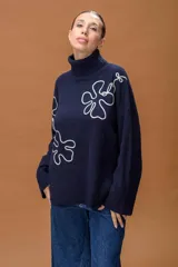 Sweater de punto color azul marino con cuello alto y diseño holgado. Presenta mangas con hombros caídos, terminaciones acanaladas y apliques de líneas orgánicas en relieve de color blanco que forman figuras florales en el frente y las mangas.