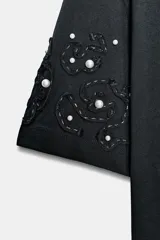 Camiseta de manga corta y cuello redondo, color negro oscuro, con detalle de bordados en forma de espiral con aplicación de abalorios y perlas en las mangas.