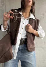 Chaleco de gamuza color chocolate con interior y bordes de corderito sintético. Presenta diseño con tachas metálicas decorativas en el frente y los hombros.