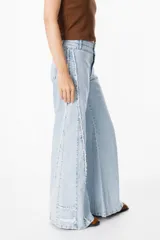 Jean color beige de corte recto, con detalles de costuras deshilachadas en los laterales y etiqueta de cuero marrón con el logo "PETRA" en la parte trasera de la cintura.