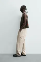 Camiseta tipo tank (sin mangas) de corte cropped fit, color gris oscuro con efecto gastado. Presenta cuello redondo y un pequeño parche rectangular con texto en la parte inferior delantera.