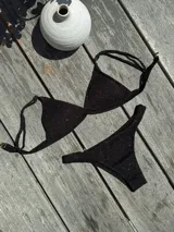 Bikini de dos piezas color marrón, con corpiño triangular fijo con corte bajo el busto, breteles regulables con hebilla y almohadillas desmontables. La bombacha es vedetina con frunce elástico en los costados.