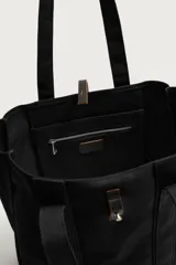 Bolso tipo shopper de algodón color negro, con asas superiores y tira de cuero con botón metálico para el cierre. Diseño amplio y versátil para uso diario.