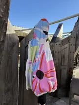 Campera oversize de gabardina combinada en colores crudo y negro, con cierre frontal y capucha de piel sintética negra. El interior está forrado en polar con diseño estampado.