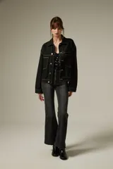 Campera de jean color negro con costuras a contratono, diseño de corte holgado, cuello camisero, cierre frontal con botones metálicos y dos bolsillos frontales con solapa.