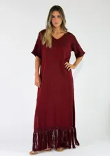 Vestido largo bordó de punto metalizado, con escote en V, mangas cortas y detalle de flecos en el ruedo.