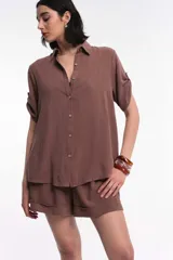 Camisa marrón de manga corta con cuello clásico y botones frontales. Las mangas tienen un detalle de presilla y botón para recogerlas.