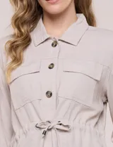 Sobrecamisa beige de lino liviano, con cuello camisero, cierre frontal de botones carey y bolsillos en el pecho. Cuenta con cordón ajustable en la cintura y mangas largas.