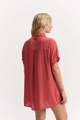 Vestido camisero corto color coral, de silueta amplia y suelta, con manga corta, cuello clásico y cierre frontal de botones.