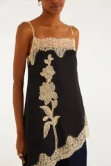 Blusa de breteles finos de color negro, con silueta amplia y caída asimétrica, confeccionada en tejido liviano con delicados detalles de encaje floral en el escote y el ruedo, y un gran aplique de encaje con diseño floral vertical en el frente.