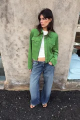 Chaqueta corta de tejido efecto ante en color verde vibrante, con cuello solapa, cierre frontal de cremallera y mangas largas. Presenta dos bolsillos frontales con solapa decorados con arandelas metálicas en el pecho.