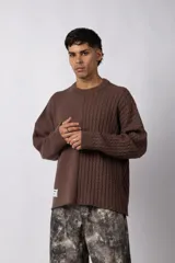 Sweater de calce relajado en color marrón, con diseño de textura combinada que presenta un lado liso y otro con tejido de ochos. Cuenta con cuello redondo y etiqueta decorativa en el ruedo.