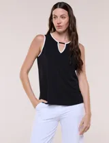 Musculosa negra de seda fría, sin mangas, con escote redondo y abertura tipo gota decorada con una placa metálica dorada. Cuenta con ribetes blancos en el cuello y las sisas, y tiene un corte evasé de calce holgado.