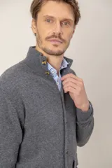 Sweater de lana lambswool color gris, con cuello alto, cierre frontal de botones y dos bolsillos delanteros tipo parche.