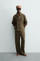 Camisa de corte relajado confeccionada en lino color verde militar, con cuello solapa, manga corta y cierre frontal de botones.