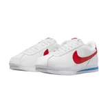Championes Nike modelo Cortez, de diseño clásico en color blanco con el logo de la marca en rojo vibrante en los laterales y talón. Presenta una entresuela con una franja azul distintiva y suela dentada para mayor tracción.