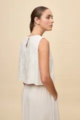 Top sin mangas color blanco con escote redondo, calce amplio y diseño con bordado floral en relieve.