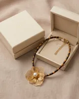 Collar con cordón de efecto carey animal print y dije central de acero bañado en oro con diseño de flor calada y perla en el centro.