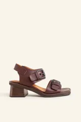 Sandalias de cuero color marrón, con taco ancho de madera y dos tiras con hebillas metálicas negras.