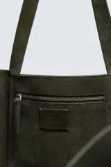 Bolso tipo shopper de gran tamaño confeccionado en piel con acabado de serraje. Cuenta con un compartimento principal abierto, un bolsillo interior con cierre de cremallera y dos asas de mano.