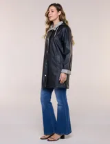Pilot engomado impermeable color azul, de corte recto estilo trench con acabado resistente al agua. Cuenta con capucha integrada, cierre frontal con broches a presión, bolsillos laterales con ojal y forro interior de tela estampada a cuadros visible en la solapa y los puños.