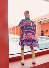 Poncho tejido con cuello alto y aberturas laterales, con diseño geométrico multicolor en tonos rosa, azul y violeta.