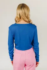 Top corto azul de tejido de punto acanalado, con mangas largas y cierre frontal con hebilla.