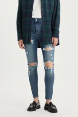 Jean de corte skinny y tiro alto, con diseño de cinco bolsillos y cierre frontal con botón y cremallera. Presenta un acabado lavado con roturas y desgastes localizados en las piernas.