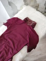 Body de lycra color bordó con cuello alto, mangas cortas y espalda descubierta. Presenta detalles de encaje en el cuello, mangas y laterales de la parte inferior. Cuenta con cierre de broches en la entrepierna.