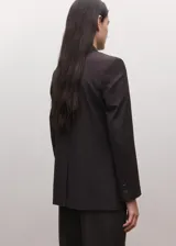 Blazer de corte sastre y diseño cruzado, con cierre de botones frontales, solapas clásicas y bolsillos laterales con solapa. Presenta una estructura entallada y hombros definidos.