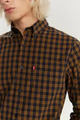 Camisa de manga larga con cuello abotonado, confeccionada en algodón con un patrón de cuadros en tonos mostaza y azul marino. Presenta un bolsillo frontal en el pecho con la etiqueta roja característica de la marca.