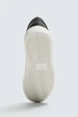 Zapatilla de cordones de caña baja, color negro, con capellada lisa y suela de goma blanca.