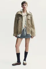 Cazadora de mujer confeccionada en piel de ante color gris oscuro con cuello subido, manga larga con trabillas en los hombros, bolsillos delanteros y con solapa en el pecho. Cierre frontal con cremallera y solapa con botones a presión.