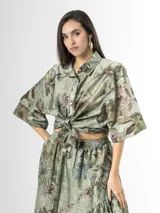 Camisa de organdí verde con estampa floral de inspiración oriental, cuello camisero, mangas cortas amplias y cierre frontal con botones.